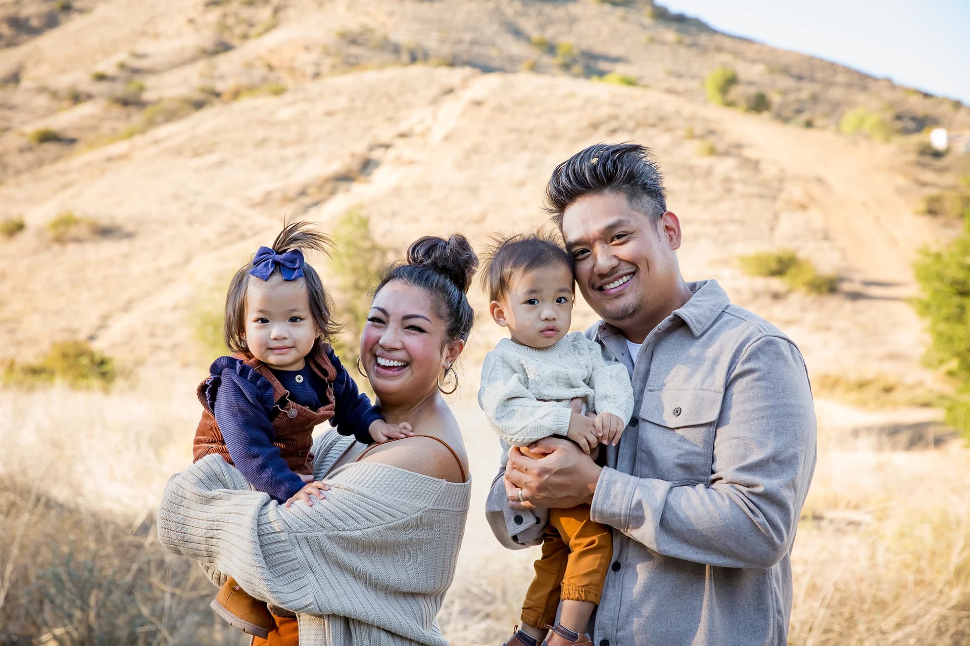 Family of four laughing together on a sunlit hillside trail